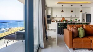 A modern living space with a balcony overlooking the ocean, a kitchen with pendant lighting, and a leather sofa.
