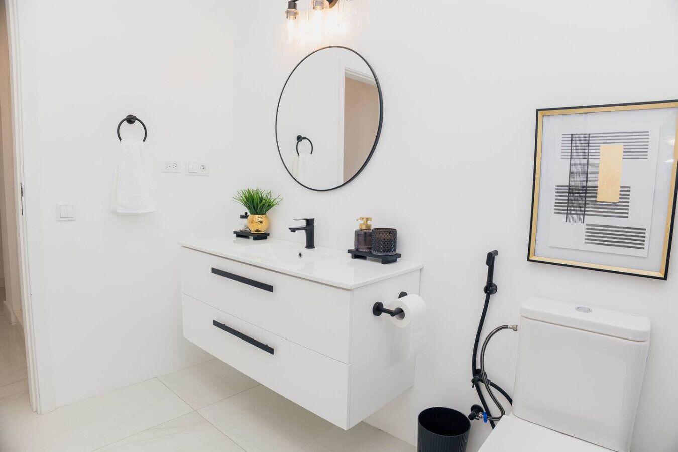 Un baño moderno con un tocador blanco, un espejo redondo, una obra de arte abstracta enmarcada y un inodoro.