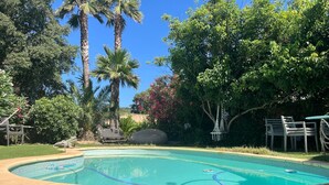 Una piscina rodeada de vegetación exuberante, con palmeras y arbustos florecientes.
