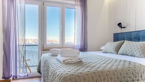 Ett sovrum med en säng, utsikt över havet genom stora fönster och en balkong.