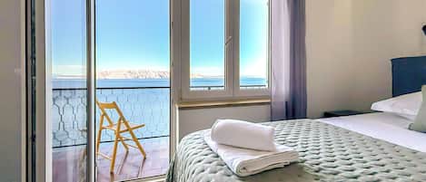 A bedroom with a bed, a chair, and a view of the sea through large windows.