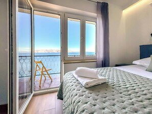 A bedroom with a bed, a chair, and a view of the sea through large windows. - Sea&Mount by Interhome (Senj)
