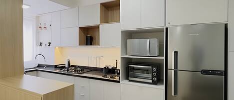 A modern kitchen with white cabinetry, a stainless steel refrigerator, a built-in oven, and a microwave.