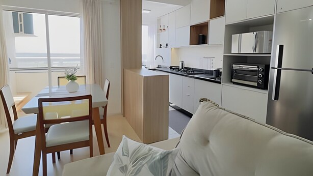 A modern kitchen with white cabinets, a built-in oven, and a dining area with a table and chairs.