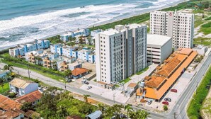 A coastal hotel with multiple high-rise buildings, a parking area, and a road leading to the beach.