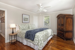 A bedroom with a bed, a nightstand, a wooden dresser, a ceiling fan, and a window with blinds.