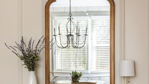 A wooden console table with a mirror, a chandelier, a vase with flowers, and a lamp.