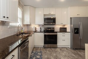 A modern kitchen with white cabinets, stainless steel appliances, and a granite countertop.