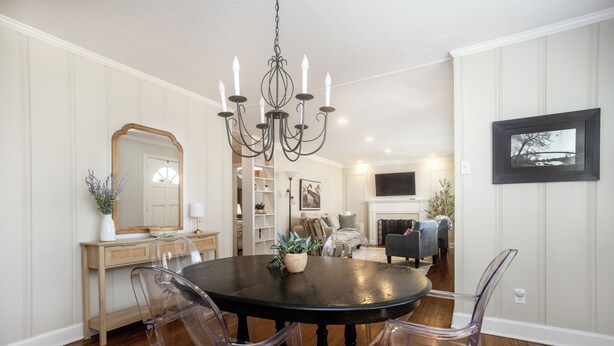 A dining area with a round table, clear chairs, a chandelier, and a mirror on the wall.
