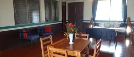 A dining area with a wooden table and chairs, a vase with flowers, and a sofa with cushions.