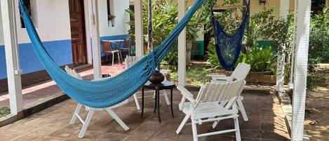 A covered patio with a hammock, white chairs, and a table.