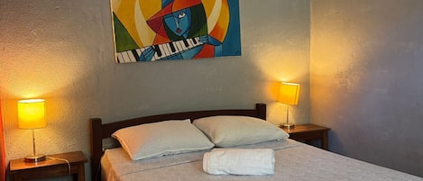 A hotel room with a bed, two bedside lamps, a painting on the wall, and a wooden nightstand.