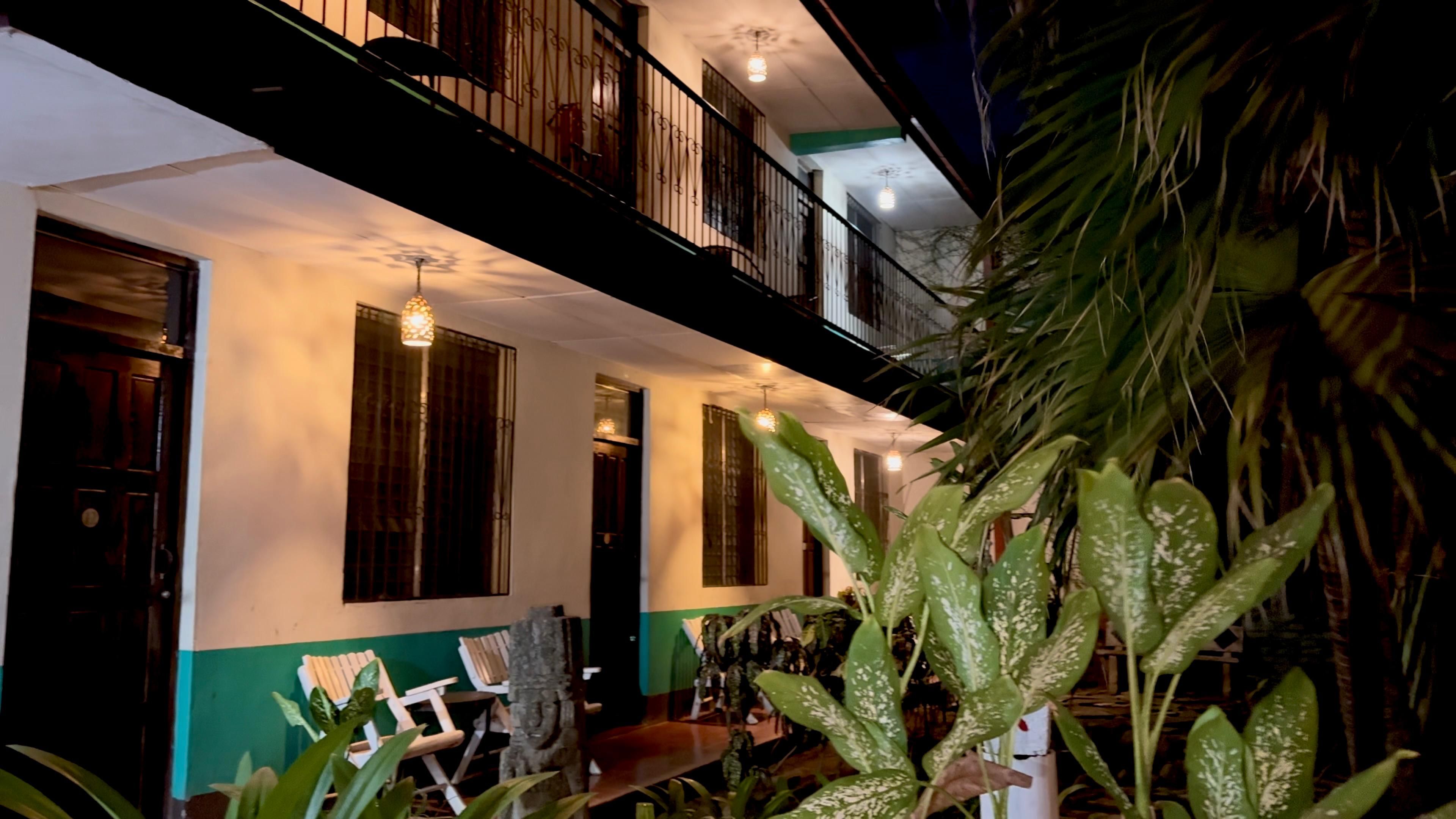 A two-story building with a balcony, a staircase, and a dining area with chairs.