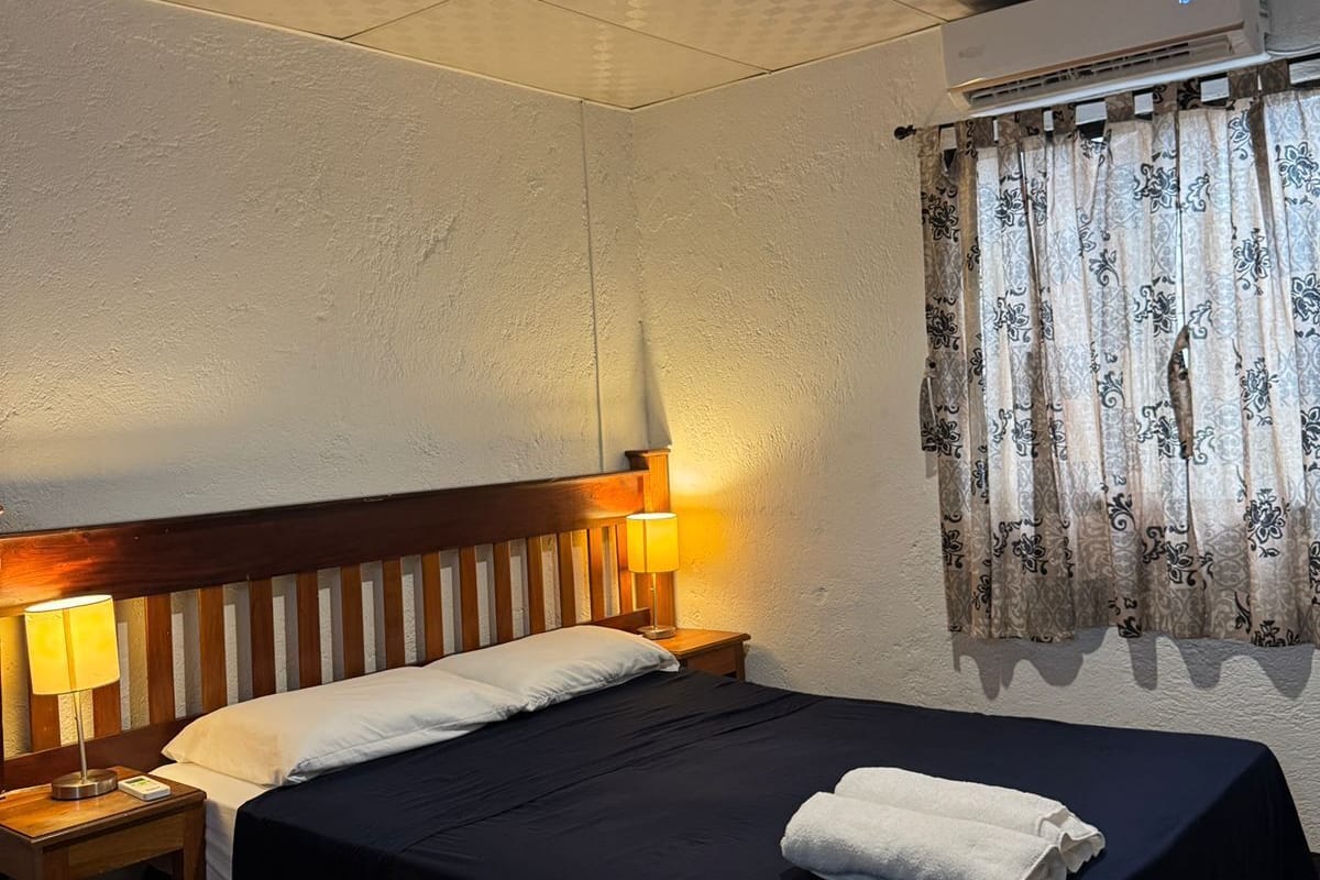 Une chambre d’hôtel équipée d’un lit, de lampes de chevet, d’une fenêtre avec des rideaux et d’un appareil de climatisation.