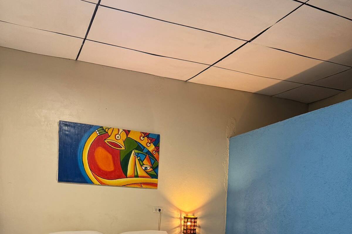 Une chambre d’hôtel avec un lit, du linge de lit blanc, un tableau abstrait aux couleurs vives accroché au mur, une table de chevet et une lampe.