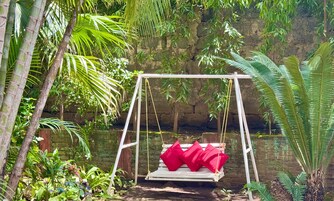 Una silla colgante con cojines rojos en un exuberante jardín.