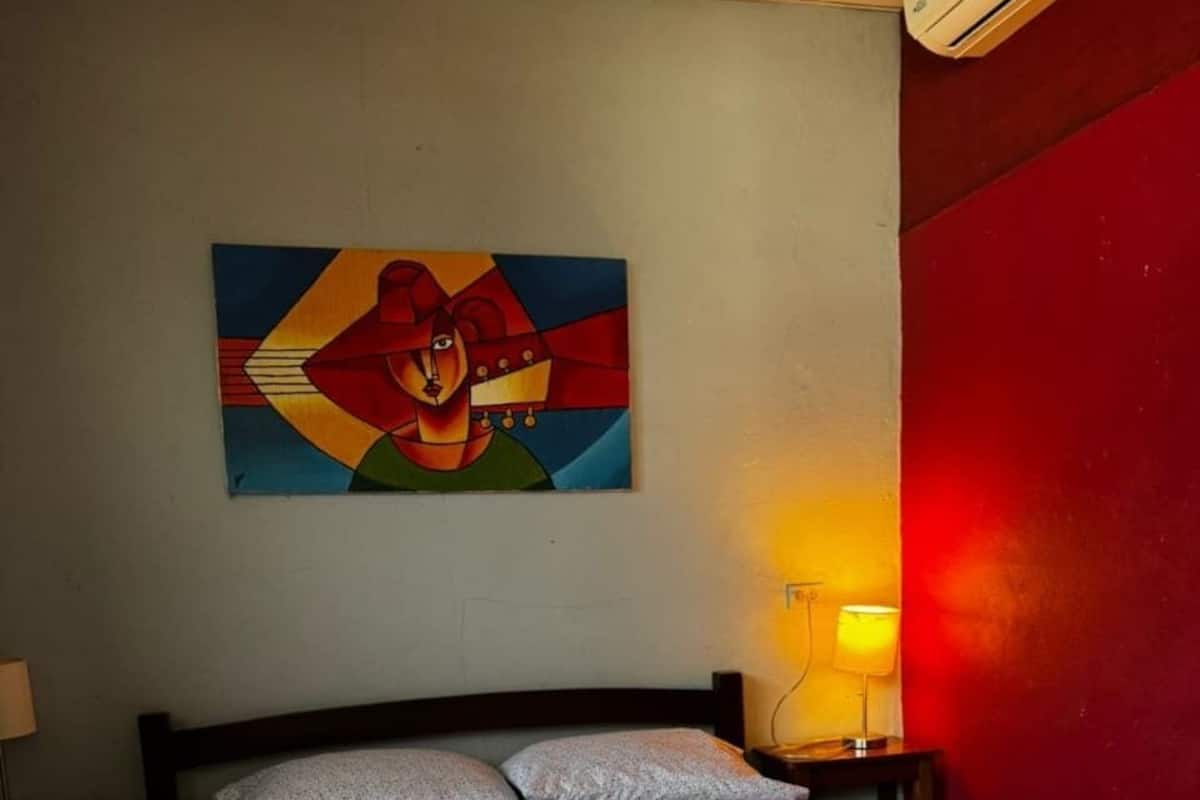 Une chambre d’hôtel avec un lit, un tableau au mur, une lampe et un mur d’accent rouge.