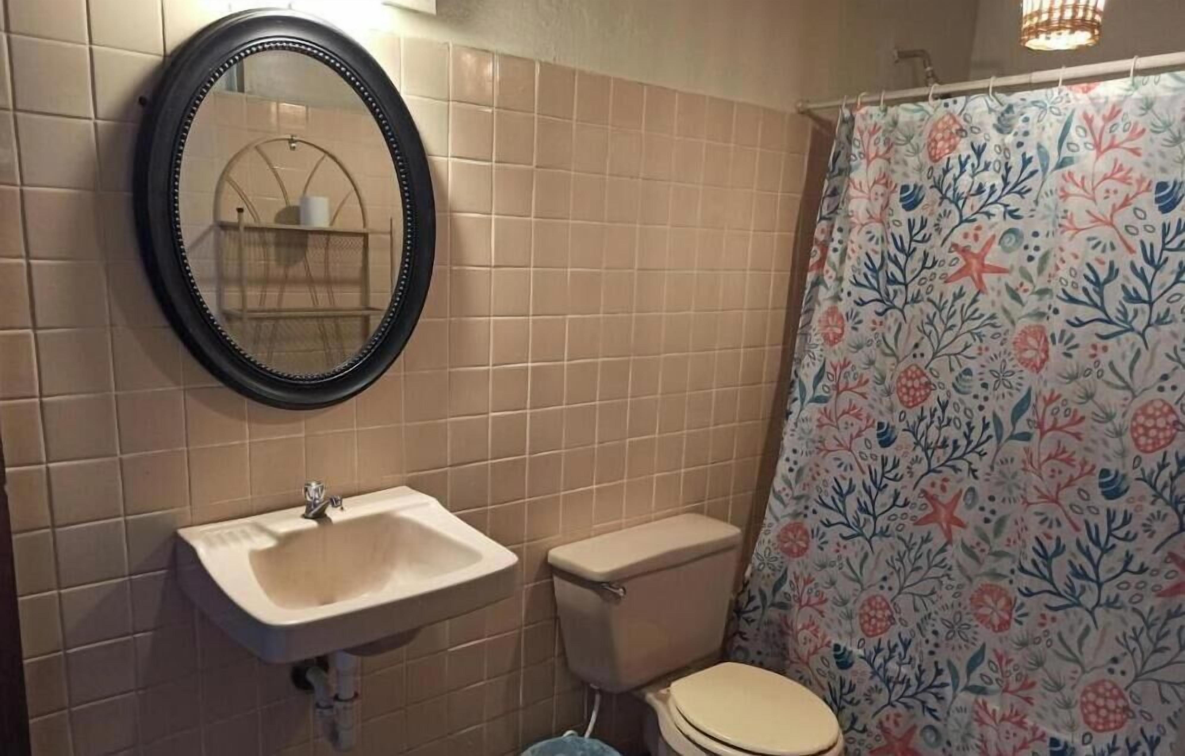 A bathroom with beige tiles, a white sink, a toilet, and a shower curtain with a floral pattern.