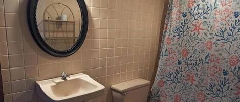 A bathroom with beige tiles, a white sink, a toilet, and a shower curtain with a floral pattern.