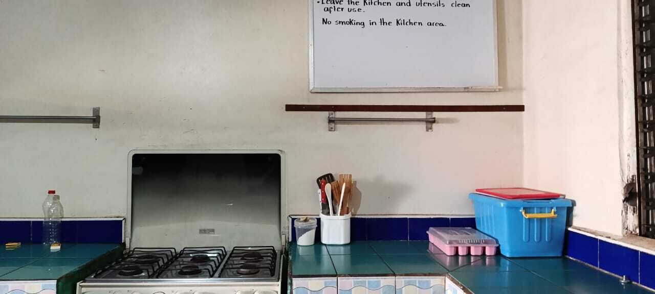 A kitchen with a stove, a whiteboard with cleaning instructions, and storage containers.