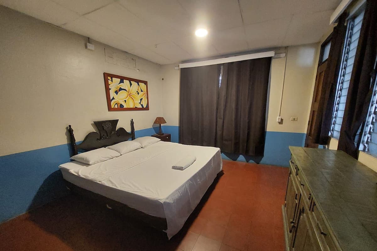 Une chambre à coucher avec un grand lit, une commode, un tableau au mur et une fenêtre avec des rideaux.