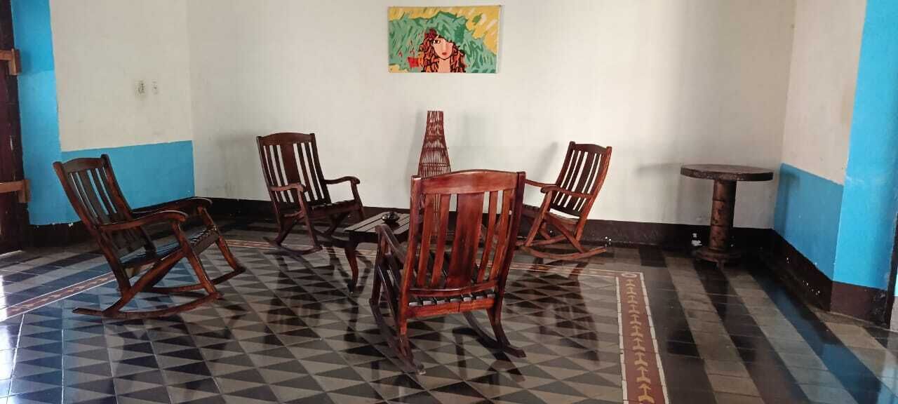 A room with a checkered floor, wooden chairs, a small table, and a painting on the wall.