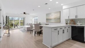 Una cocina moderna con armarios blancos, una isla central y un comedor con vistas.