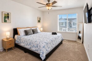 A bedroom with a bed, a nightstand, a ceiling fan, a window with blinds, and a wall-mounted TV. - Elevated Urban Retreat | Views | Sleeps 7 + Pet (Riverton)