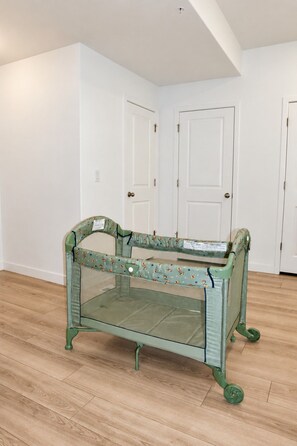 A room with a green baby playpen in the center, white walls, and wooden flooring.