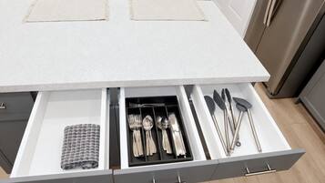 A kitchen with a white countertop, a stainless steel refrigerator, and a drawer organizer with utensils.