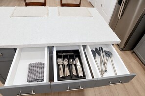 Una cocina con encimera blanca, refrigerador de acero inoxidable y organizador de cajones con utensilios.