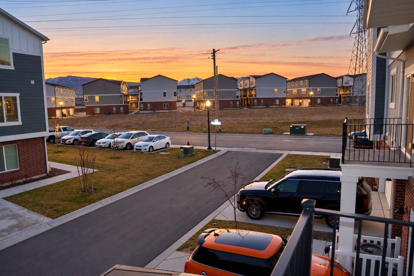 A residential area with multiple two-story houses, a parking lot with several cars, and a clear sky during sunset.