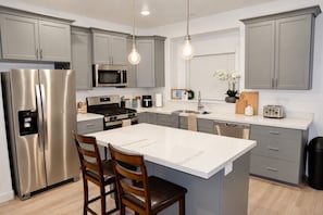 Una cocina moderna con electrodomésticos de acero inoxidable, una isla central e iluminación colgante.