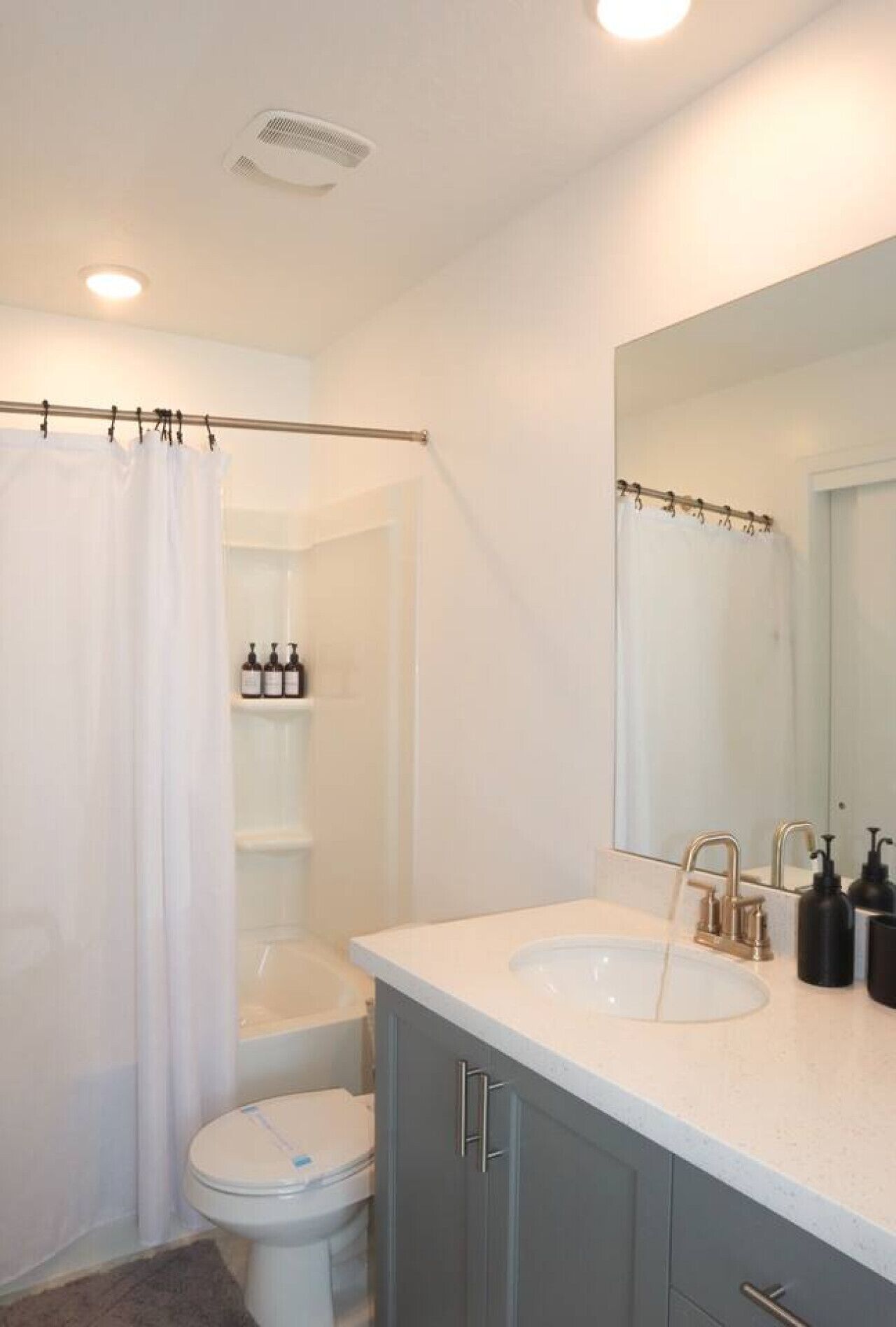 A bathroom with a shower curtain, a toilet, a sink with a mirror, and toiletries on a shelf.