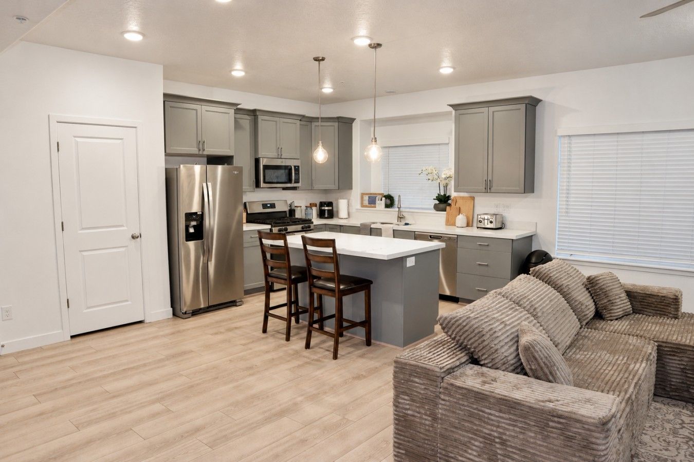 A modern kitchen with grey cabinets, stainless steel appliances, and a central island with bar stools.