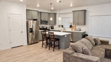 A modern kitchen with grey cabinets, stainless steel appliances, and a central island with bar stools.
