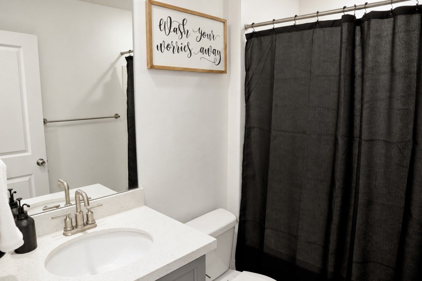 A bathroom with a white sink, a mirror, a black shower curtain, and a motivational quote on the wall.