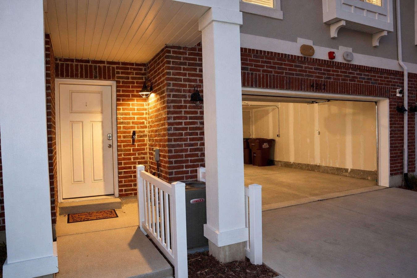 Un garage residenziale con una porta bianca, un muro in mattoni e un recinto bianco.