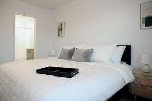 A neatly made bed with a tray, a bedside table with a lamp, and a window with curtains.