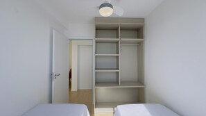Een slaapkamer met twee eenpersoonsbedden, een garderobe met meerdere planken en een plafondventilator.