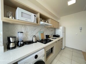 A kitchen with a microwave, coffee maker, blender, kettle, and a built-in oven. - Solarium Beach Club -Apartamento T1.1003 (Itapoá)