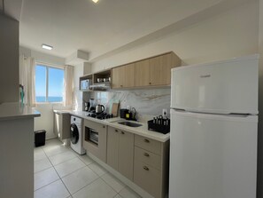 A modern kitchen with a built-in washing machine, a refrigerator, and a microwave. - Solarium Beach Club -Apartamento T1.1003 (Itapoá)