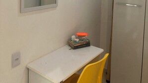 Et lille værelse med et hvidt skrivebord, et spejl, en gul stol og et garderobeskab.