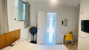 Et hotelværelse med en seng, et skrivebord med stol, et fjernsyn, en ventilator og en dør til et udendørs område.