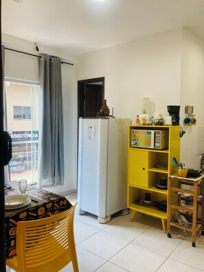 A compact kitchen with a refrigerator, a yellow shelving unit, and a dining area with a table and chairs. - Complete apartment behind the Shopping Mall (Belém)