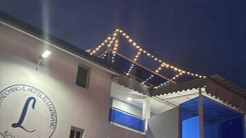 Un edificio con un grande insegna luminosa a forma di 'L', diversi balconi e una porta blu.