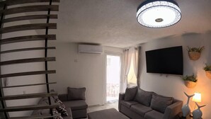 Un salon moderne avec un escalier en colimaçon, un ensemble de canapés gris, un téléviseur à écran plat et un luminaire suspendu au plafond.