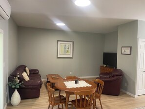 A living room with a dining table, two sofas, a TV, and artwork on the wall.