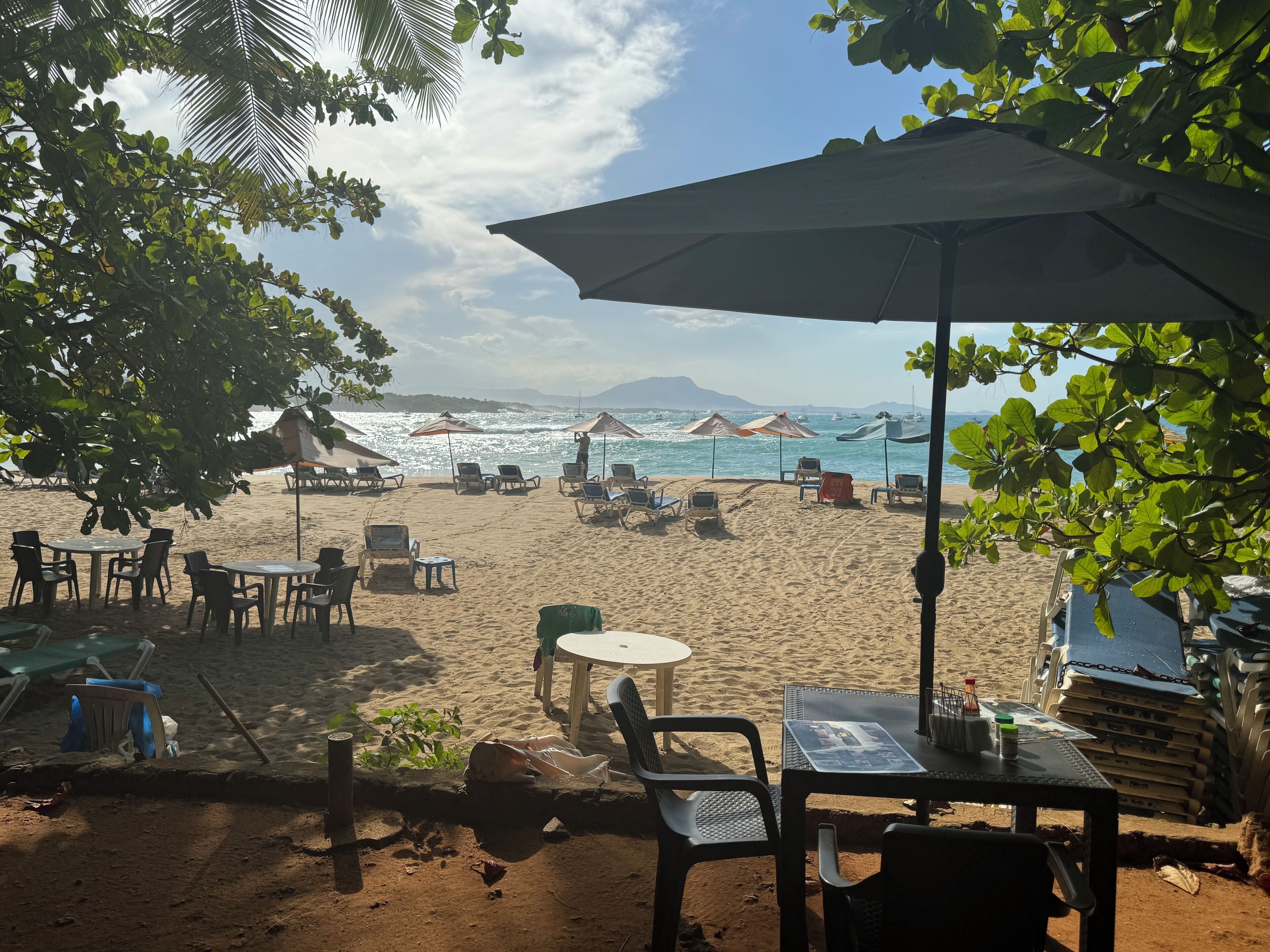 A beachside seating area with tables and chairs under umbrellas, overlooking the sea.