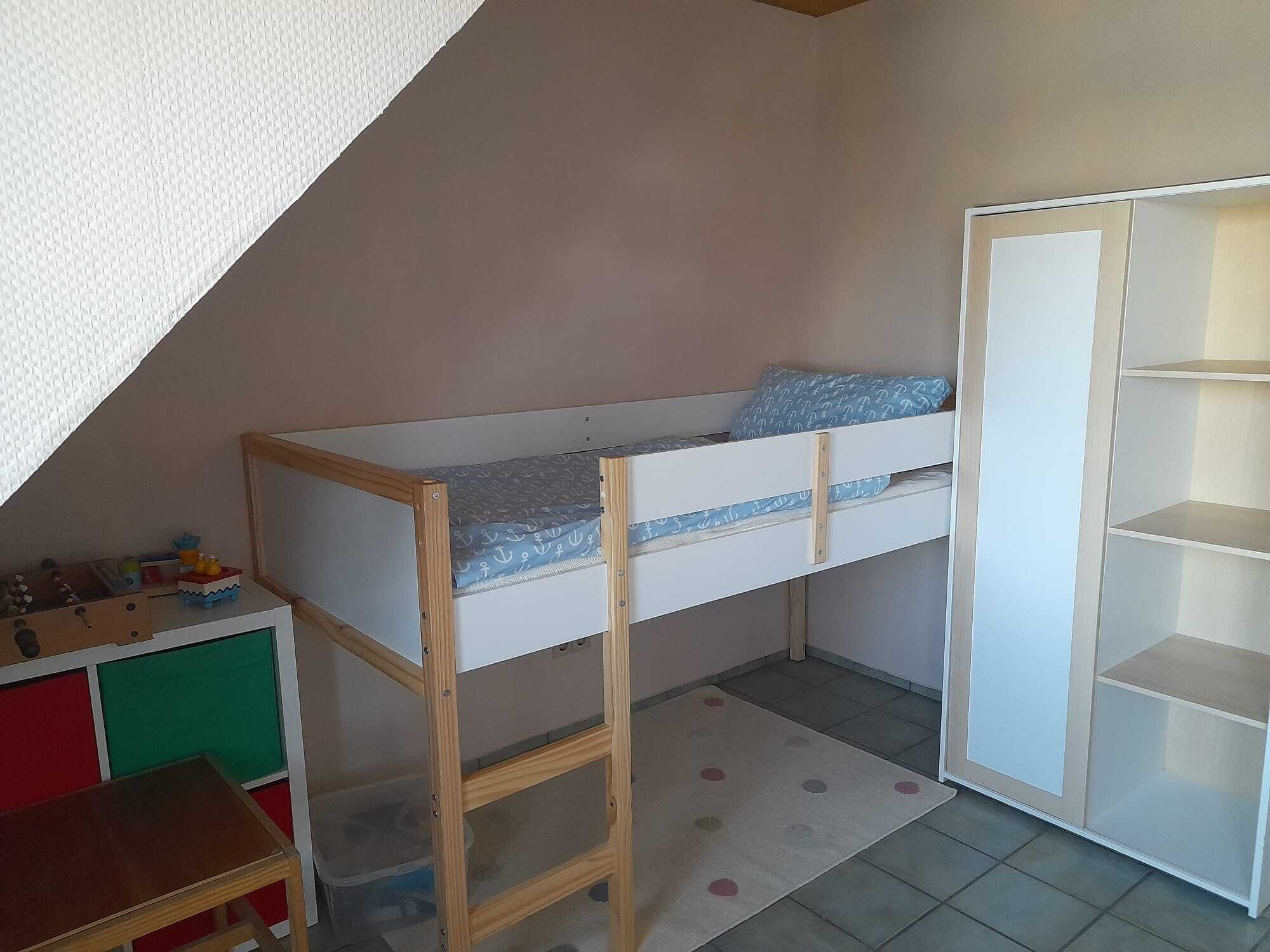 A bunk bed with a wooden ladder, a small desk, and a wardrobe with open doors.